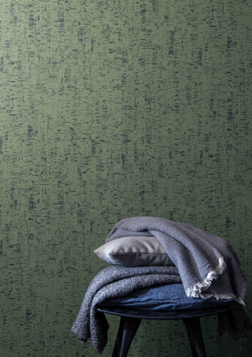 La collection de revêtements muraux High Performance Patina d'Omexco allie performance, durabilité et esthétique moderne. Sur le mur de ce mini-décor, nous voyons le motif "Clay", inspiré des murs en argile et d'une ancienne technique de peinture qui consiste à étaler un mince enduit de chaux sur le mur à l'aide d'un pinceau. La superbe couleur verte du mur crée une atmosphère naturelle et sereine. Devant le mur se trouve une table d'appoint noire sur laquelle sont posés des oreillers et des couvertures moelleux.