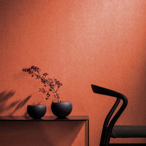 Revêtement mural orange vif contrastant avec une chaise noire et deux vases ronds foncés sur une console en métal. Branche avec des baies.