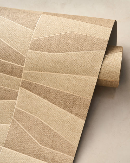 Un gros plan d’un rouleau de papier peint déroulé de la collection Oase, mettant en avant la référence OAS231, Domino. Ce design propose une mosaïque de tissage en papier, habilement façonnée à partir de formes géométriques qui apportent un effet visuel dynamique. Le motif structuré repose sur un support métallique, disponible en or ou en argent, ajoutant une brillance subtile et une profondeur à la texture. Les tons neutres et terreux soulignent la beauté naturelle du matériau, renforçant l’esthétique organique de la composition.