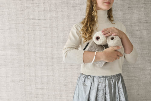 Une composition contemporaine et élégante mettant en avant la collection Pure d’Omexco, référence PU251, nommée Delicate. Ce papier peint associe gracieusement du raffia fin à des fils métalliques subtils, créant un jeu de textures naturelles et chatoyantes. Le tissage complexe reflète une élégance raffinée, en faisant un point central pour les intérieurs modernes. Au premier plan, une femme portant un pull à col roulé crème et une jupe métallisée argentée tient des bobines de fil et un échantillon de tissu, mettant en valeur l’essence tactile et artisanale du design. Les tons harmonieux du papier peint créent une ambiance sereine et luxueuse, idéale pour les espaces qui embrassent la sophistication et l’artisanat.