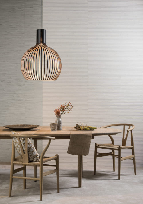 Table en bois d'aspect naturel avec deux chaises Wegner en forme de triangle. Un cadre parfait pour les revêtements muraux naturels Shades of Pale d'Omexco.