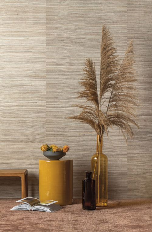 Nous voyons ici un intérieur mettant en vedette notre sisal polychrome de la collection de revêtements muraux Seraya : des fils de sisal inégaux multicolores, tissés et laminés sur un fond réfléchissant. Nous l'avons associé à une table jaune, un vase ocre et de grands panaches.