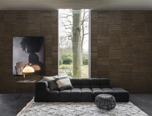 Salon avec un fauteuil anthracite, un tapis luxuriant et un pouf rond. Au mur, une photo d'une jeune fille avec une coupe afro. Les murs sont habillés d'écorce de bananier tressée : l'élégance de ce matériau naturel est le fruit du travail minutieux d'un artisan expérimenté qui ramasse l'écorce de bananier dans les climats tropicaux. La collection Omexco Seraya.