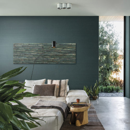 Intérieur vert d'une chambre à coucher avec sol en béton. Lit avec des oreillers assortis, près du sol. Revêtement mural Aruba sur le mur. Sur le mur, une œuvre d'art représentant un nénuphar de la même collection de revêtements muraux.