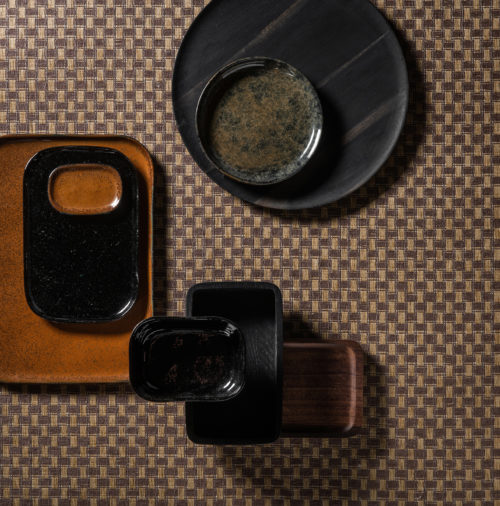 Revêtements muraux "Twist" de la collection Tribu d'Omexco. S'inspirant d'anciennes techniques japonaises, notre papier est teint ou imprimé, coupé en rubans, torsadé en fils et enfin tissé pour créer des textures raffinées. Ici, nous voyons une composition intéressante avec des assiettes en céramique et de superbes revêtements muraux en papier tissé dans des tons terreux.